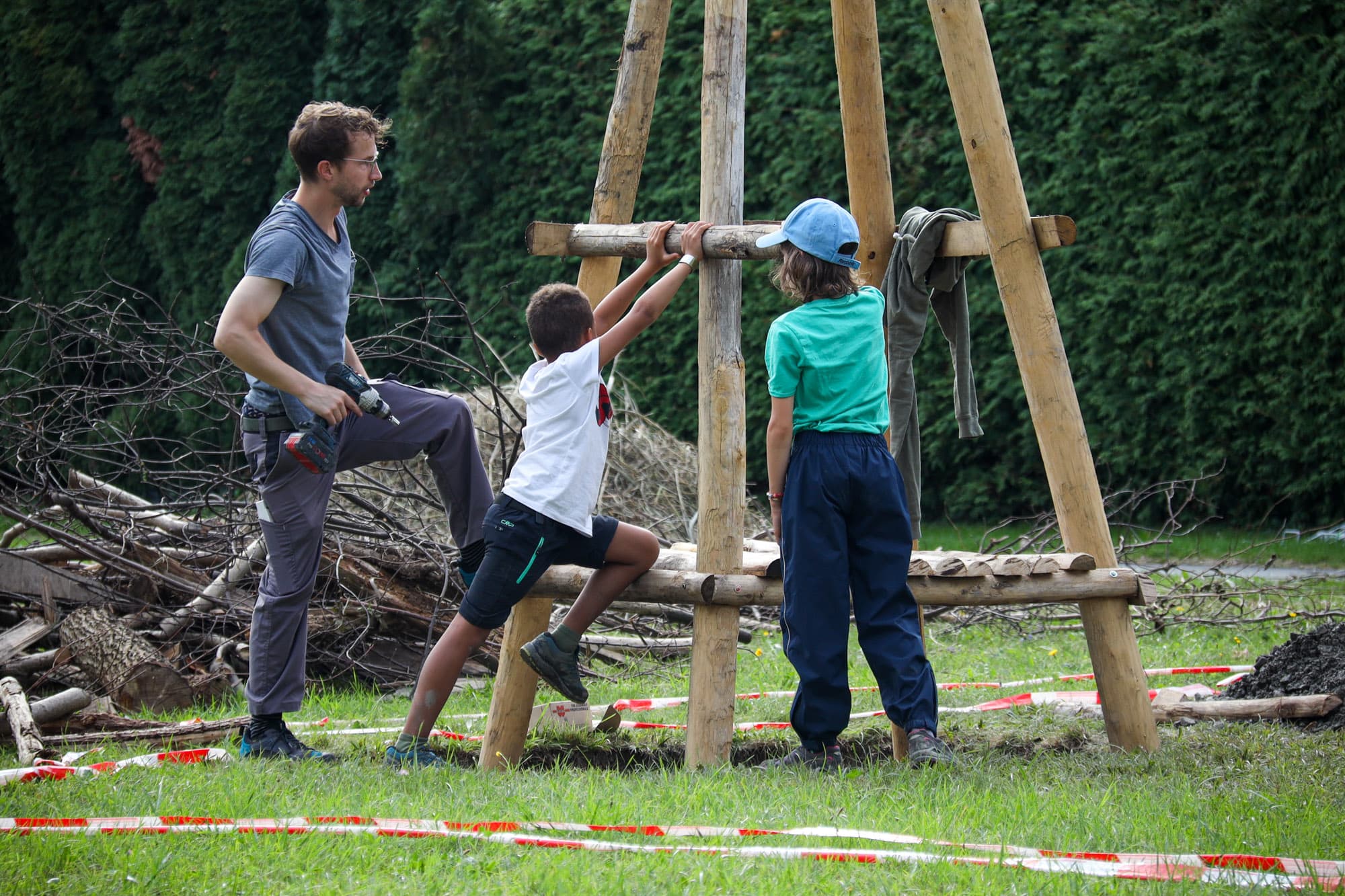 Zwei Kinder und ein Lehrer arbeiten an einem Lebensturm auf dem Schulgelände.